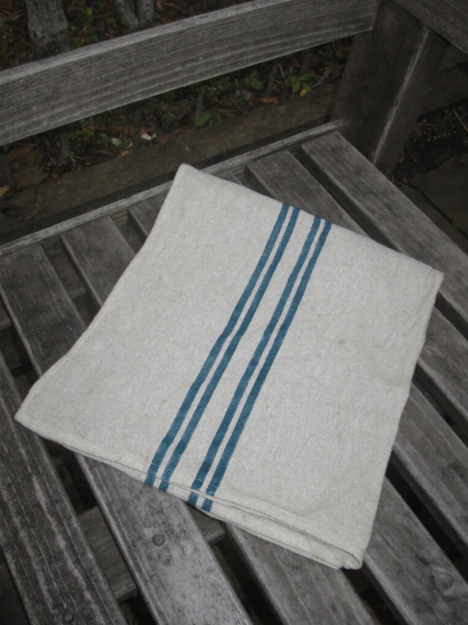 Linen-Cotton Towel in Teal Stripe, folded on a wooden garden bench