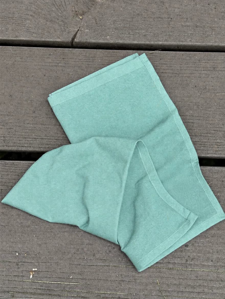Plain Weave Towel in Sea Glass, folded on a wooden garden bench