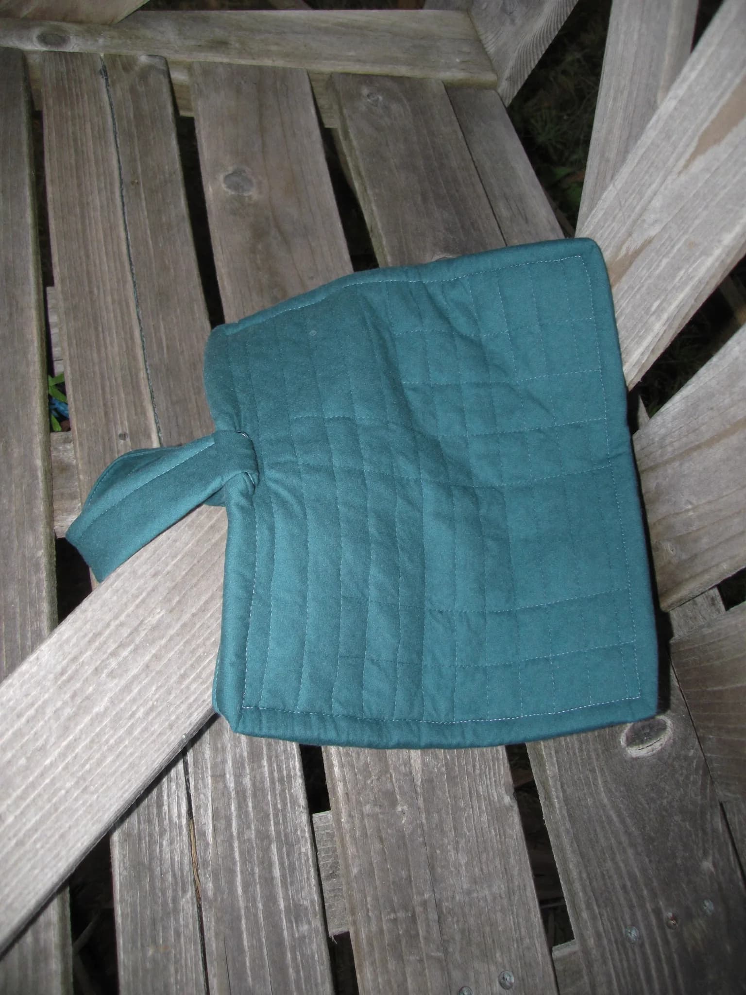 Quilted Pot Holder in Deep Teal, folded on a wooden garden bench