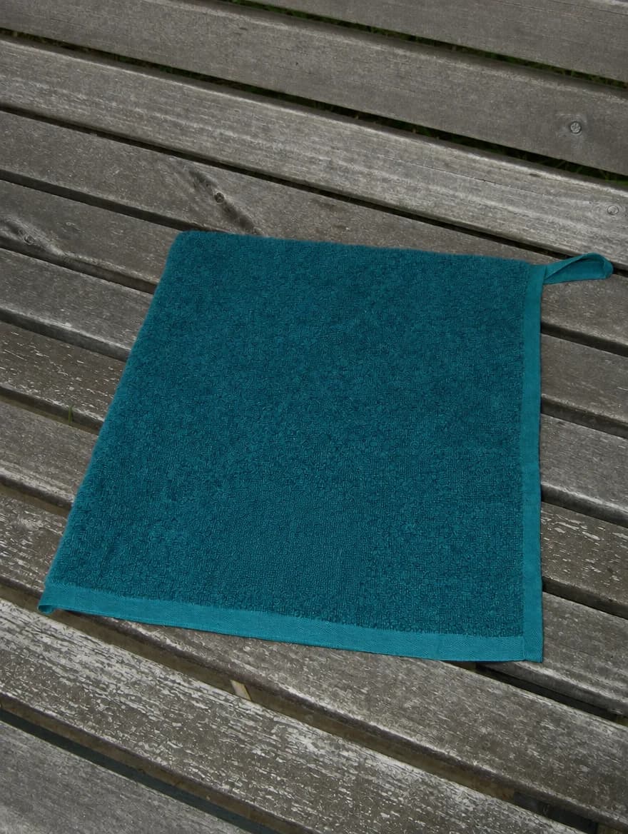 Waffle Towel in Deep Teal, folded on a wooden garden bench